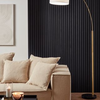 A living room with a wood panelled wall in black and a beige sofa