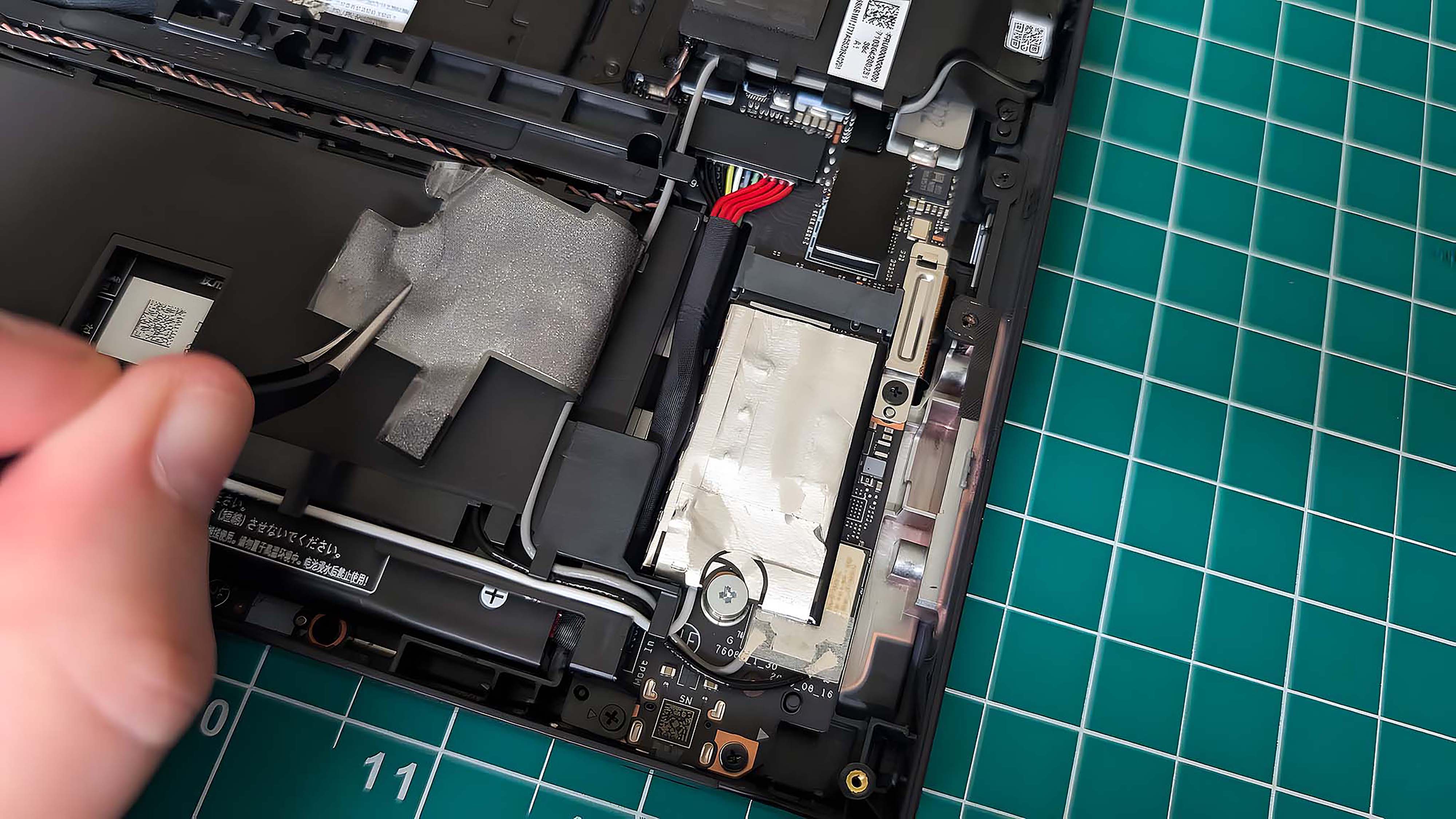 A hand using tweezers to pull back the battery sticker from over the Lenovo Legion Go SSD.
