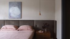 A mid-century style bedroom with a large brown headboard, a wooden nightstand, and a red and white striped bedding set