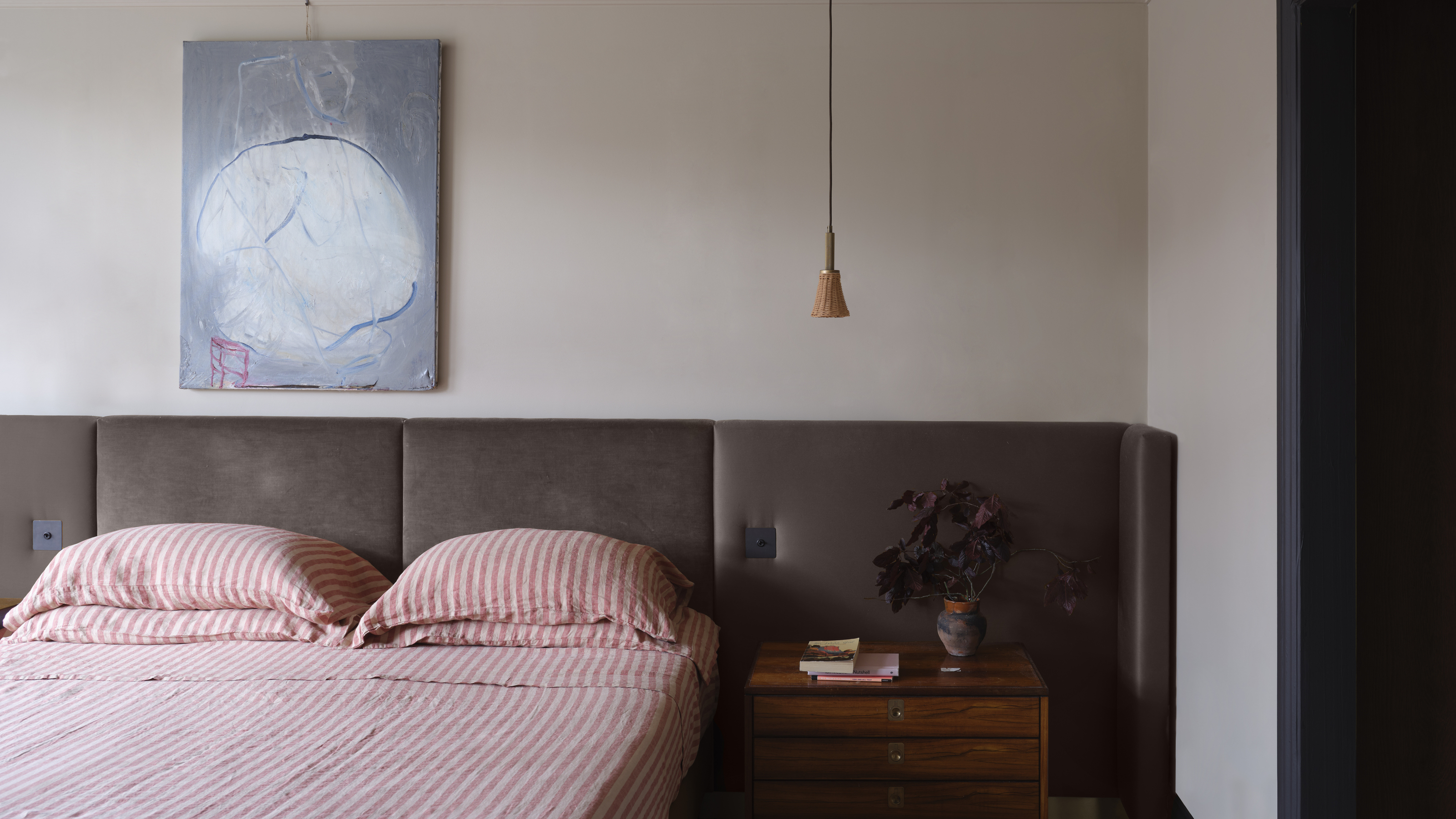 A mid-century style bedroom with a large brown headboard, a wooden nightstand, and a red and white striped bedding set