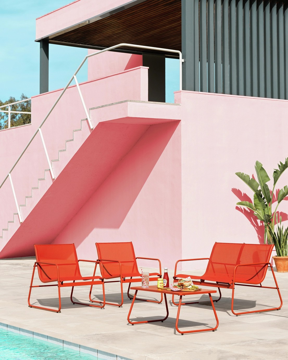 Image of an orange outdoor furniture set on a poolside patio outside of a modern house, painted light pink.