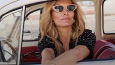 A close up of a female model wearing a polka dot black dress and sunglasses from Cotton Traders, in a retro car.