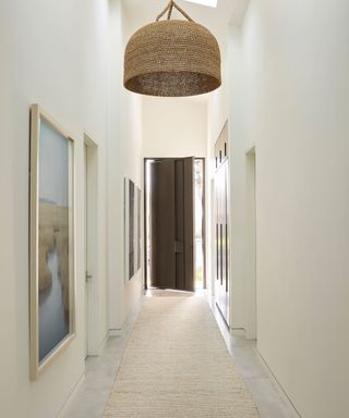 Calming cream hallway, corridor with wall-mounted artwork, large pendant light, cream runner.
