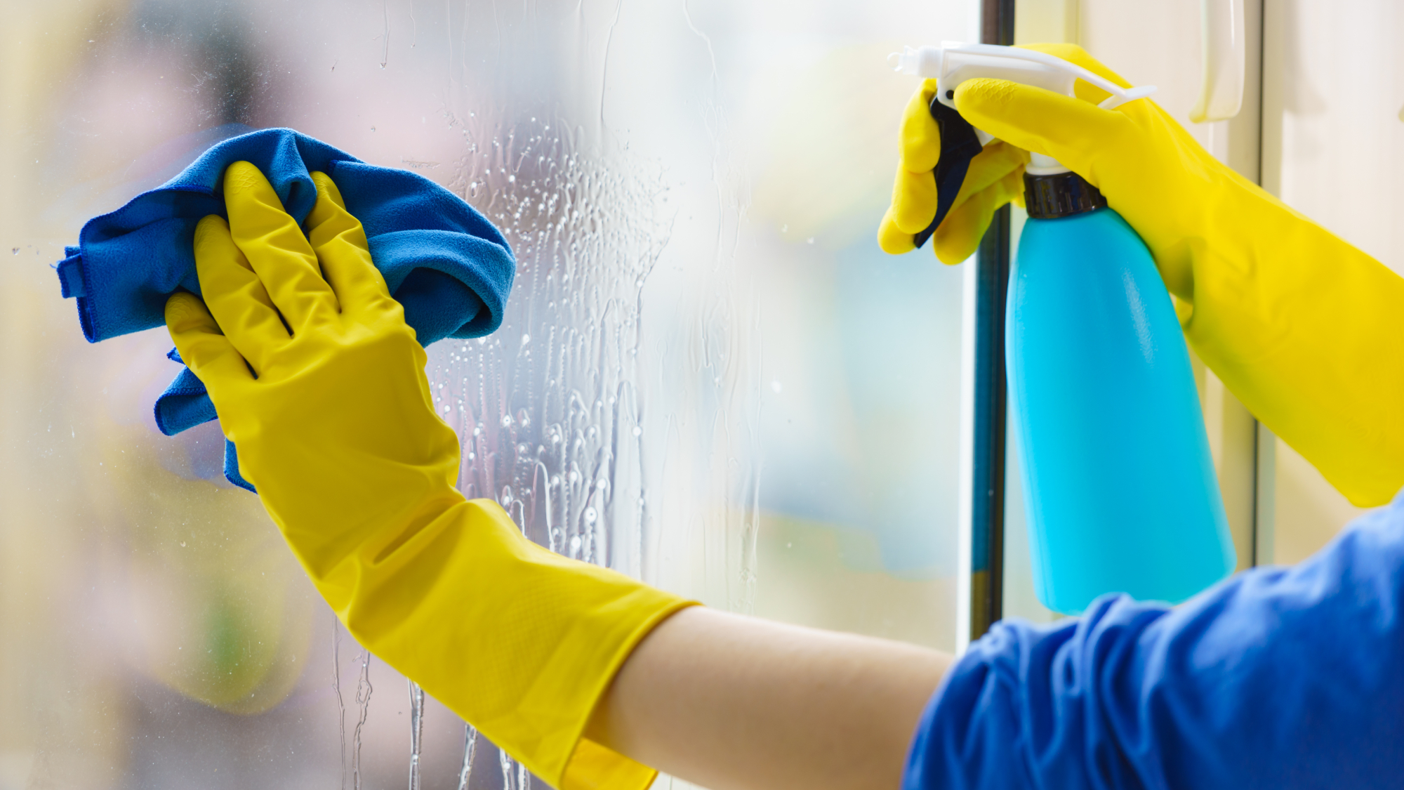 person cleaning window using blue cloth and spray bottle