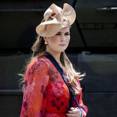 Princess Catharina-Amalia wearing a red dress and beige hat with her arm in a sling