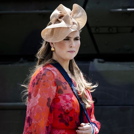 Princess Catharina-Amalia wearing a red dress and beige hat with her arm in a sling