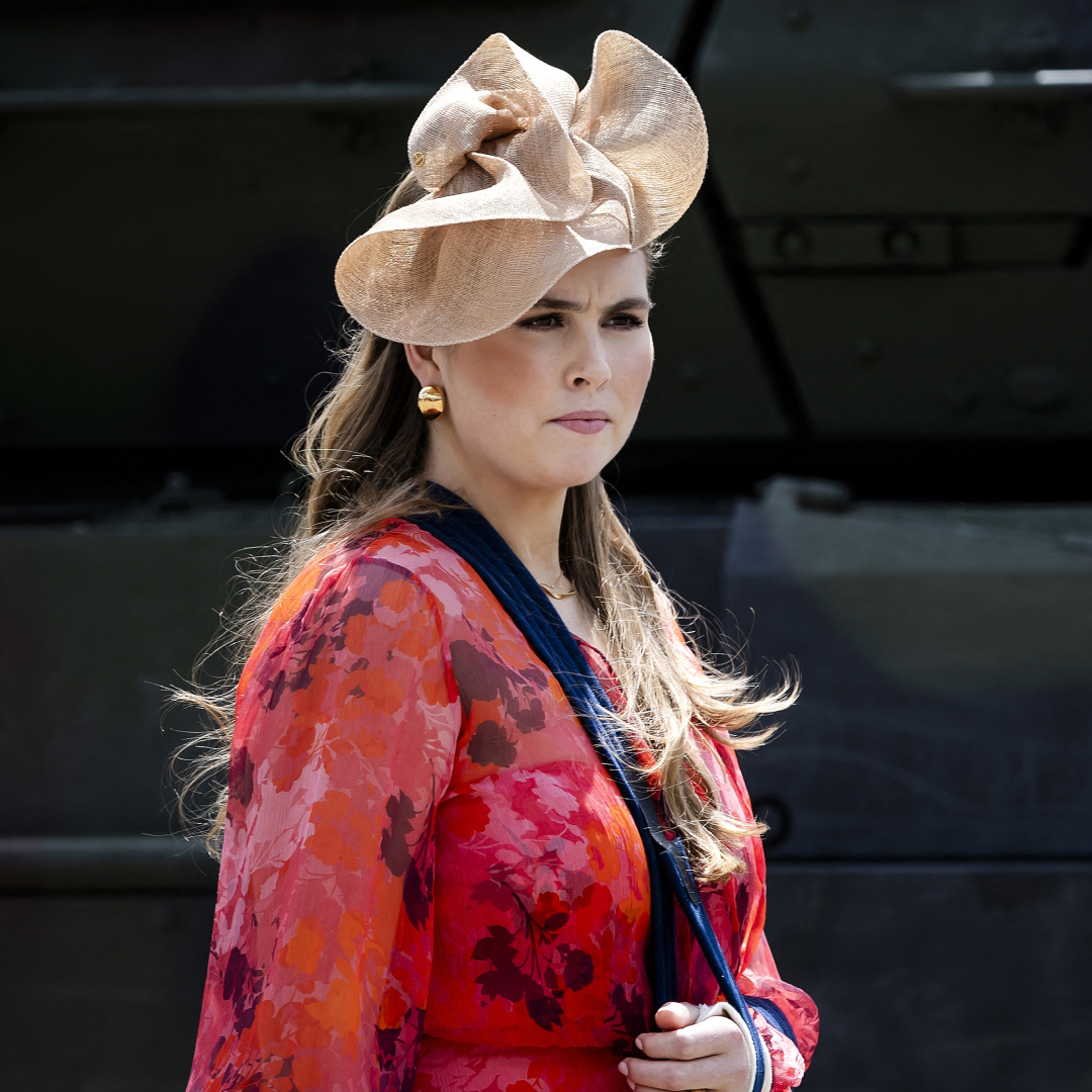 Princess Catharina-Amalia wearing a red dress and beige hat with her arm in a sling