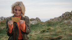 Millie Gibson as Ruby Sunday in Doctor Who looks down at a piece of paper on a remote cliff in Wales.