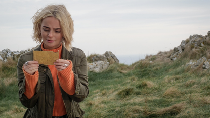 Millie Gibson as Ruby Sunday in Doctor Who looks down at a piece of paper on a remote cliff in Wales.