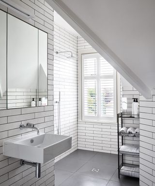 A wet room with white metro wall tiles with black grouting and a sloped ceiling, shower storage