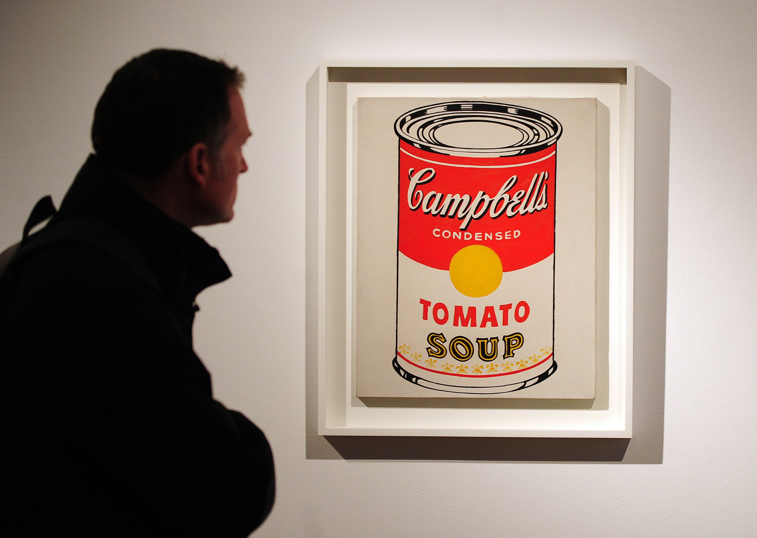 Andy Warhol's tomato soup painting hanging on a white wall with a man next to it