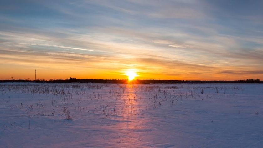 the sun shines low on the horizon, bathing the snowy winter landscape in a soft orange glow.