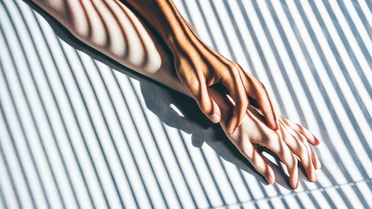 Man and woman&#039;s arm, placed on on top of the other on surface against sunlight backdrop creating shadow lines across their arms, representing how to have a better orgasm through deep breathing together