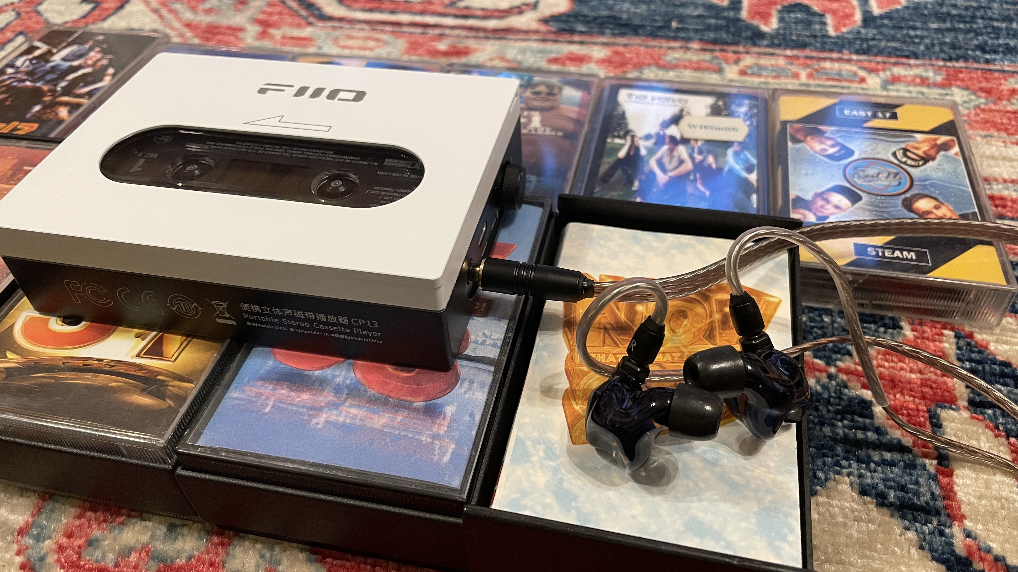FiiO's CP13 with Campfire Audio Clara IEMs, on top of several cassette tapes, all on a colorful carpet