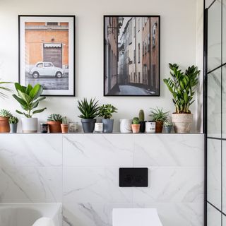 White marble tiled bathroom with pot plants and pictures on the wall