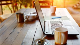 Workstation with laptop and coffee cup set up on garden table depicting remote working