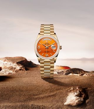rolex watch with orange face against beach backdrop