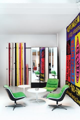Two white round tables with three green chairs next to big poster