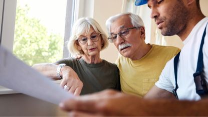 Mature couple examining blueprints with manual worker during home renovation process. 