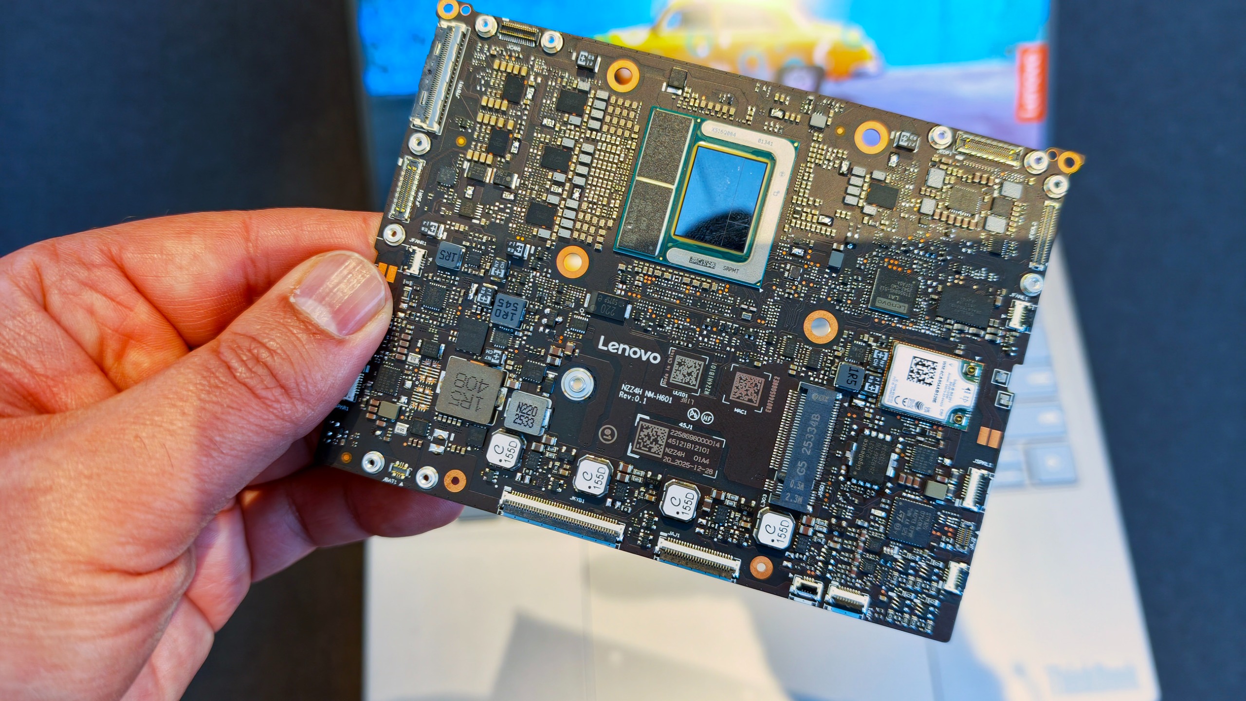 Hand holding a compact, highly integrated square laptop motherboard branded with the Lenovo logo.