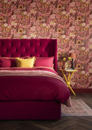 maximalist bedroom with dark pink bed, bold floral wallpaper, yellow side table, yellow cushion