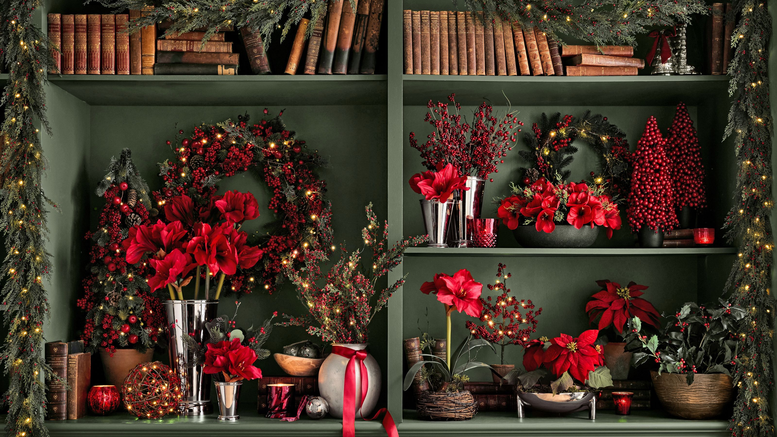 Pottery Barn's Christmas faux foliage in red and green displayed in a green bookcase