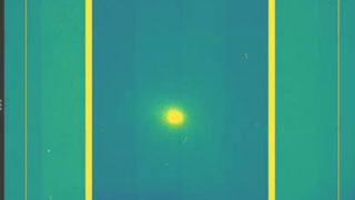 A screenshot of a yellow dot which is comet 3I/ATLAS in the middle of a green and purple background