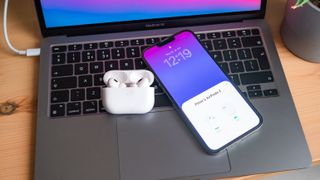 A set of AirPods Pro and an iPhone 13 Pro Max on the keyboard of a MacBook Air