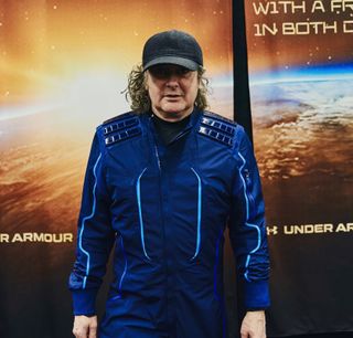 a man standing wearing a hat and blue jumpsuit