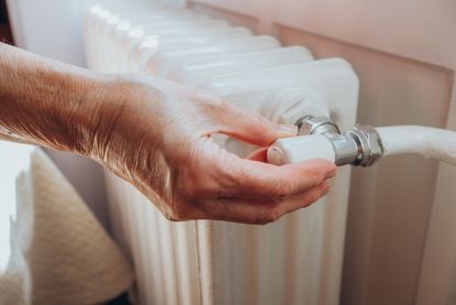 Senior woman adjusts dial on radiator