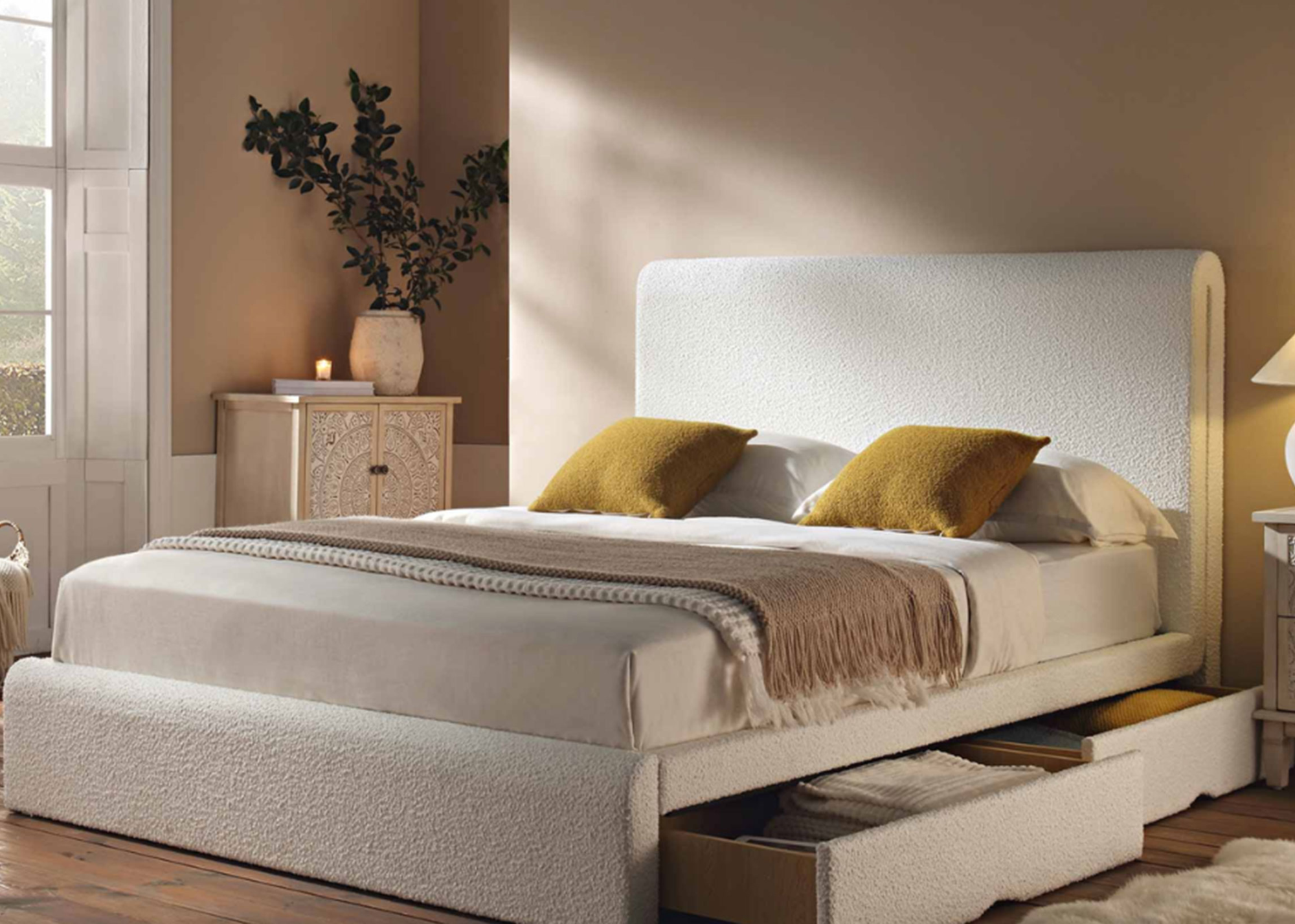 a bedroom with a bed with under bed storage with the two drawers slightly open in a white boucle fabric against a pale dusty pink wall