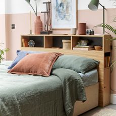 A bedroom with a shelved storage headboard, pink wall and green bedding