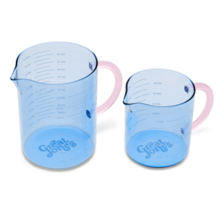 A pair of blue tinted glass measuring cups with light pink handles