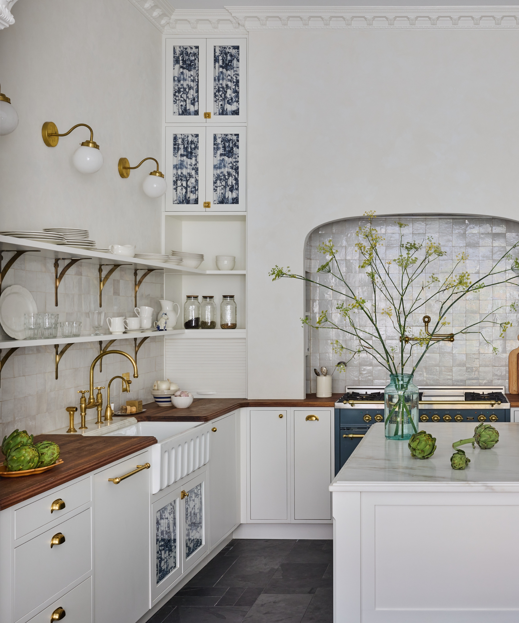 A white kitchen with wood countertops and glazed cabinets lined with pleated fabric