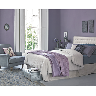 lilac and grey bedroom with purple walls, white bed and duvet cover, purple throw and cushions, grey armchair and grey carpet