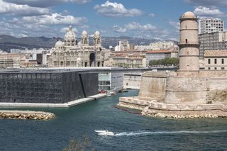 The seafront of Marseille, one of the best foodie cities in France. The Cathedral Fort and Mucem building Marseille harbour with a speedboat jetting past