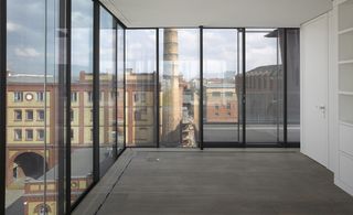A bare space with floor to ceiling glass walls with black panels and grey carpet and views of the city