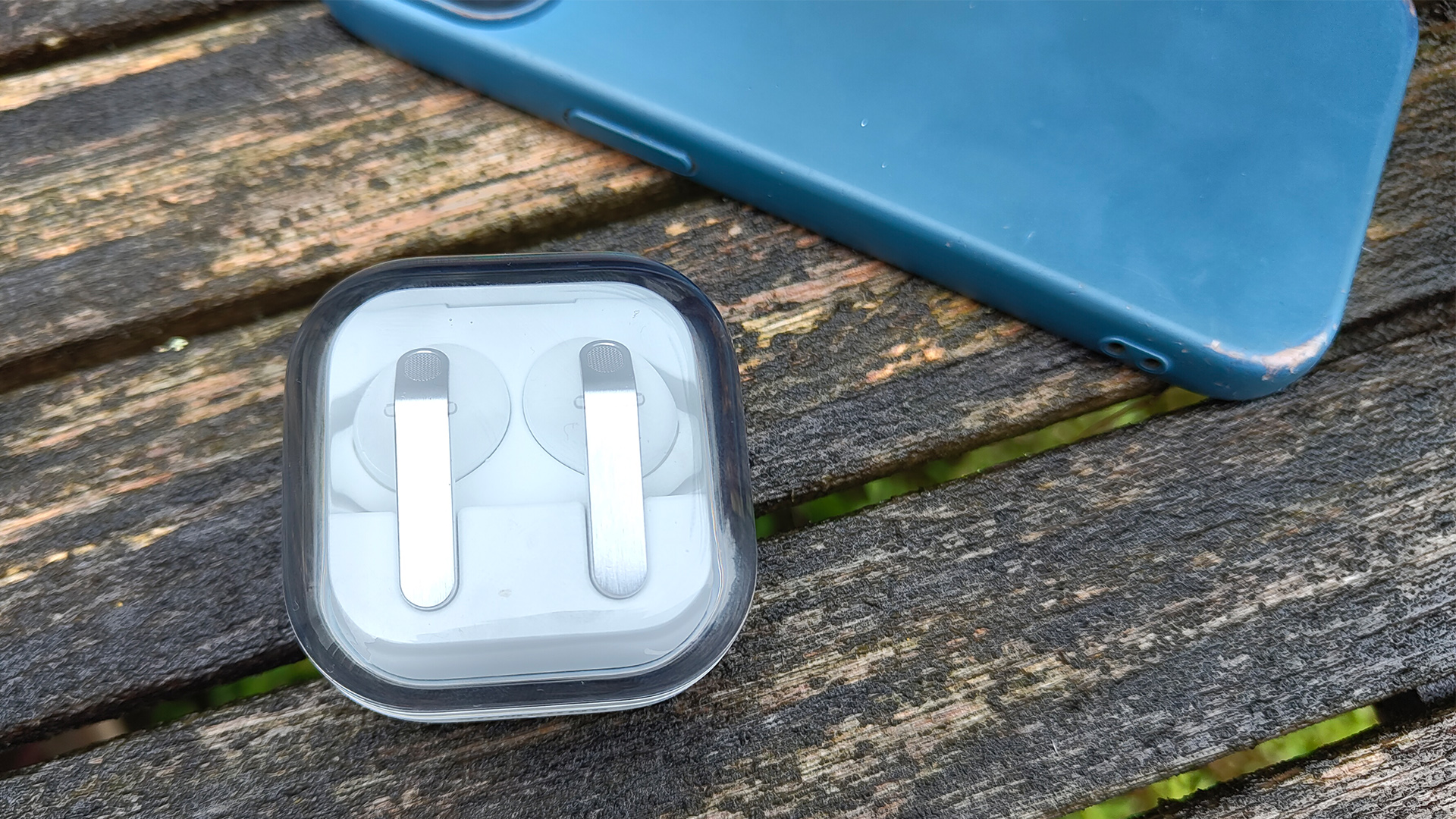Samsung Galaxy Buds 4 Pro wireless earbuds on wooden garden furniture in closed case next to blue phone