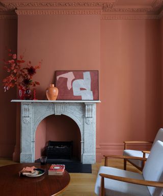 terracotta living room, colored walls, window and plinth, wooden floor, marble fireplace, artwork, round coffee table, two wooden upholstered armchairs, vases, side table, Farrow & Ball