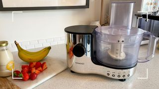 Food processor in kitchen next to chopping board with bananas, strawberries and milk ready to use: how to use a processor guide