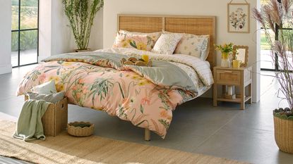 A bedroom with floral sheets on the bed and scalloped wicker accessories placed around the room