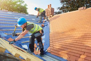 Builders fixing tiles to a roof