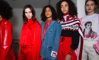 Model wears a bright red silk shirt, another wears a denim blazer whilst others are dressed in a logo T-shirt and knitted jumper