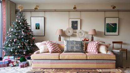 Christmas tree trends. Modern living room with large sofa decorated with cushions, geometric rug, wide christmas tree beside window