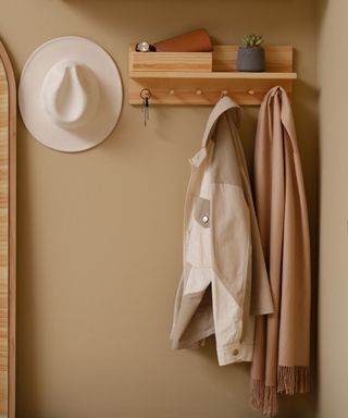 A brown small entryway with a wooden shelf with coats hung up on it and a hat next to this