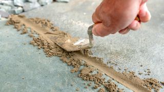 Hand with pointing trowel smoothing out sandy mortar mix between grey patio slabs