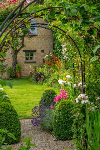 archway with climbing plants over it leading to the lawn and the cotswold house