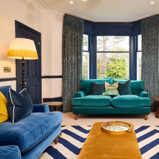 Living room with navy skirting, mustard ottoman and blue-green sofa