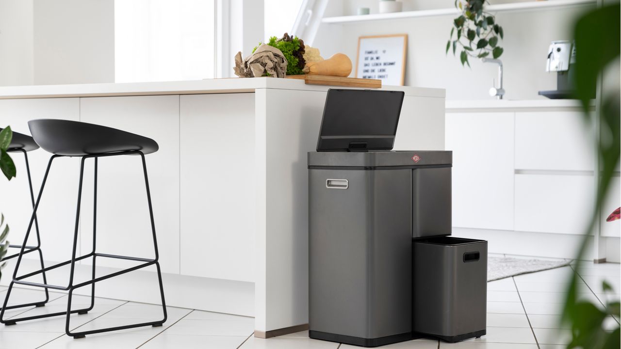 A modern white kitchen with slim black bar stool and grey recycling trash cans