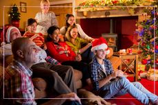 A family watching TV next to a Christmas tree